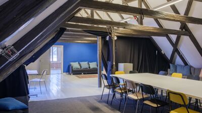 Loftsrom med synlige takbjelker, bord, stoler og sittegrupper til møter, workshops eller kreative aktiviteter.