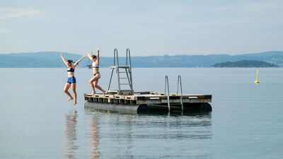 To jenter som hopper fra flytebrygge i vannet