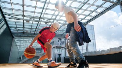 To gutter som spiller basket inne i solen under glasstak