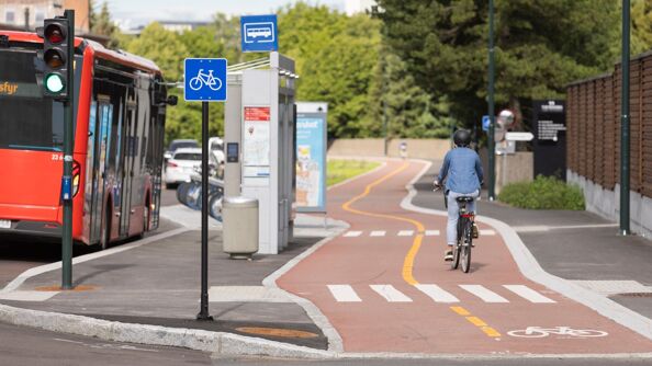Syklist med ryggen til på en tofelts sykkelvei. Sykkelveien ligger på innsiden av et busstopp, der en rød buss har stoppet.