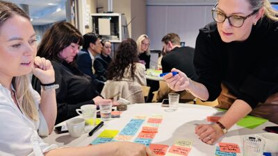 Flere mennesker sitter rundt et bord. På bordet ligger det lapper i ulike farger med tekst som blir diskutert.