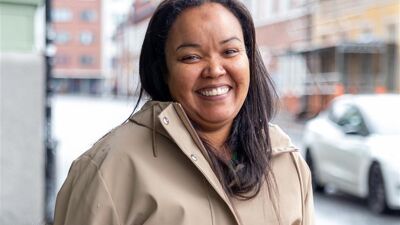 Suad Isse Mohammad fra Uteseksjonen står på gaten. Hun har beige frakk på seg og smiler.