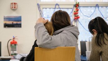 Tre personer som sitter med ryggen til. To av personene, et voksen og et barn, sitter på samme stol. Den voksne holder rundt barnet.