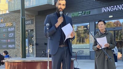 Lokalpolitiker Mudassar Mehmood snakker i mikrofon. Etatsdirektør for Bymiljøetaten, Gerd Kjørven, står bak.