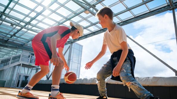 To unge gutter i en skolegård i lek med en basketball.