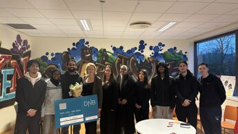 Oppstilt bilde med 9 ungdommer og byråden i midten. De holder opp en stor sjekk og smiler mot kamera.