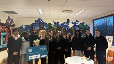 Oppstilt bilde med 9 ungdommer og byråden i midten. De holder opp en stor sjekk og smiler mot kamera.