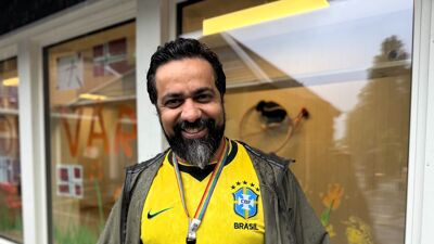 Smilende mann med gul t-skjorte foran vindu. Regnvåt.