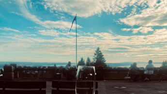 Utsikt mot lettskyet himmel og flaggstang med vimpel fra uteserveringen på Frognerseteren.
