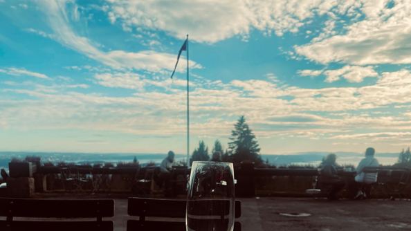 Utsikt mot lettskyet himmel og flaggstang med vimpel fra uteserveringen på Frognerseteren.