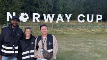 Tre utekontakter foran et skilt med Norway Cup