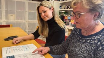 To kvinner sitter og blar sammen i brosjyren "Digital trygghet- En veileder for eldre i en digital hverdag
