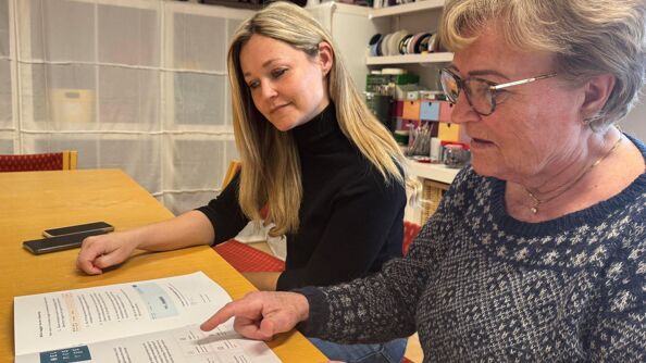 To kvinner sitter og blar sammen i brosjyren "Digital trygghet- En veileder for eldre i en digital hverdag