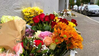 Flere blomsterbuketter og lys på et fortau.