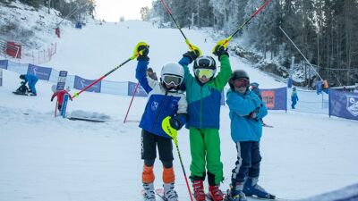 Tre barn i i alpinutstyr på bunnen av en skibakke