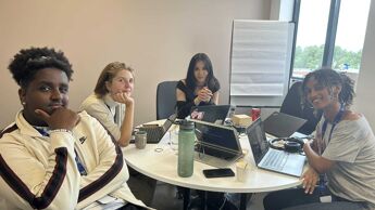 Fire ungdommer som sitter inne på ett kontor og arbeider. Alle smiler foran kamera.