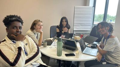 Fire ungdommer som sitter inne på ett kontor og arbeider. Alle smiler foran kamera.