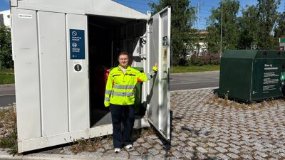 Dame i gul jakke stående i døråpningen til en grå container.