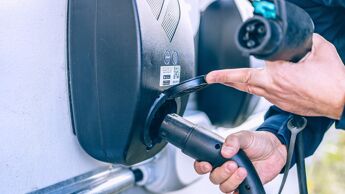 Nærbilde av en hånde som putter en ladekabel inn i en ladestasjon.