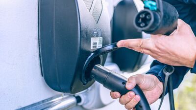 Nærbilde av en hånde som putter en ladekabel inn i en ladestasjon.