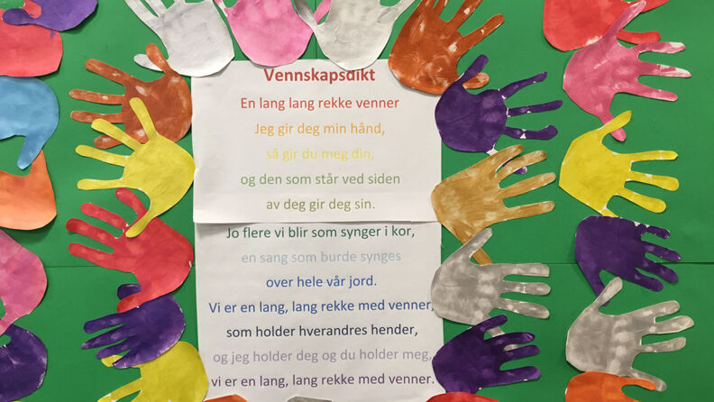 Dikt hengt opp på veggen med grønn bunn, omgitt av hender i flere farger