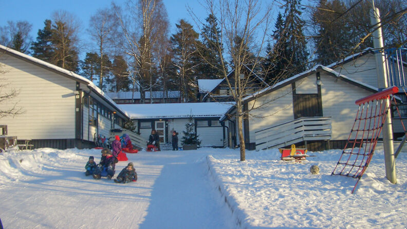 Uteområde med barn som aker ned gangveien, hvitmalt barnehage i bakgrunnen 