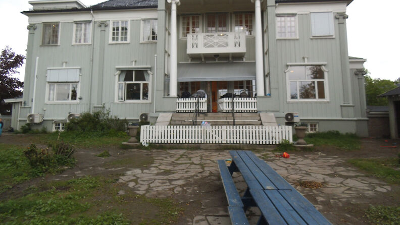 Fasaden av barnehagen,  pistasjfarget villa med stakittgjerde foran inngangen og to benker utenfor 