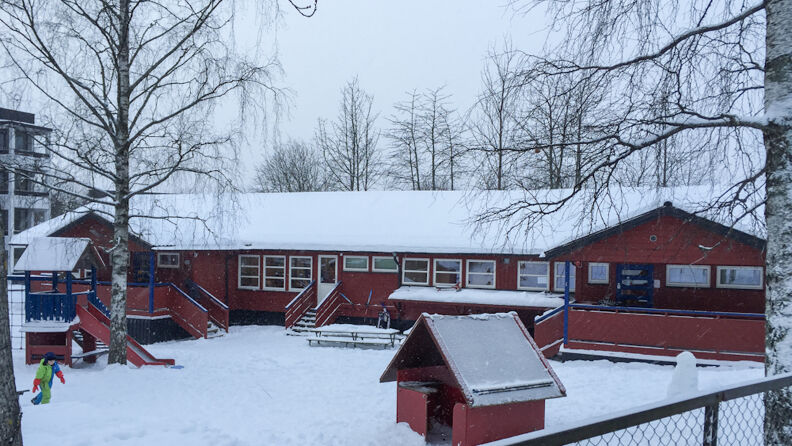 Uteområde med klatretårn med sklie, benker og trær rundt, i  vinterlandskap