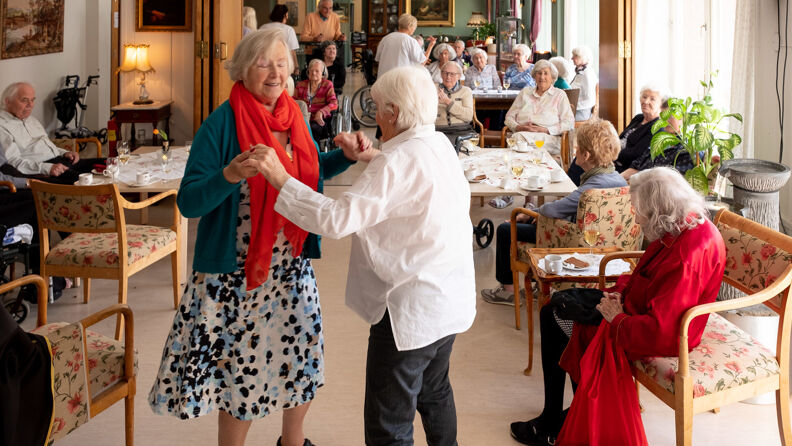 To eldre damer danser i en dagligstue