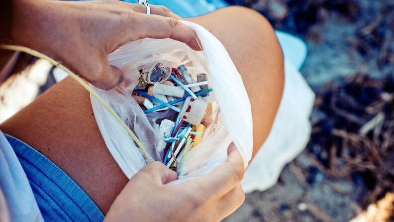 Nærbilde av en plastpose hvor det er samlet små biter plastsøppel, holdes åpen mot en kvinnes lår.
