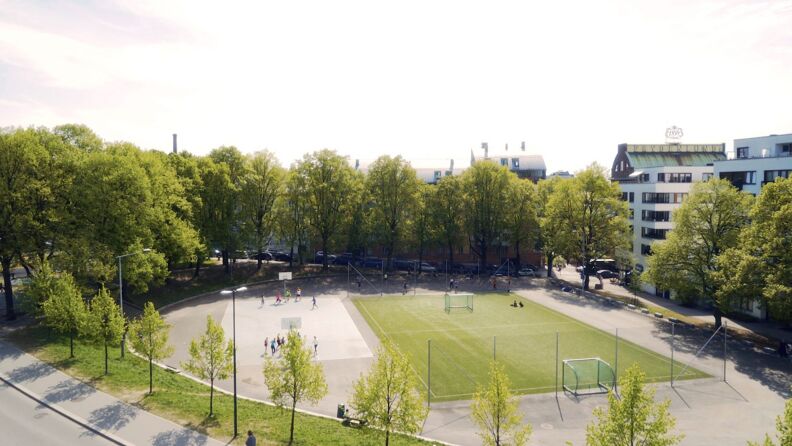 Oversiktsbilde over fotballbanen til høyre og basketballbanen til venstre omringet av trær og blokker