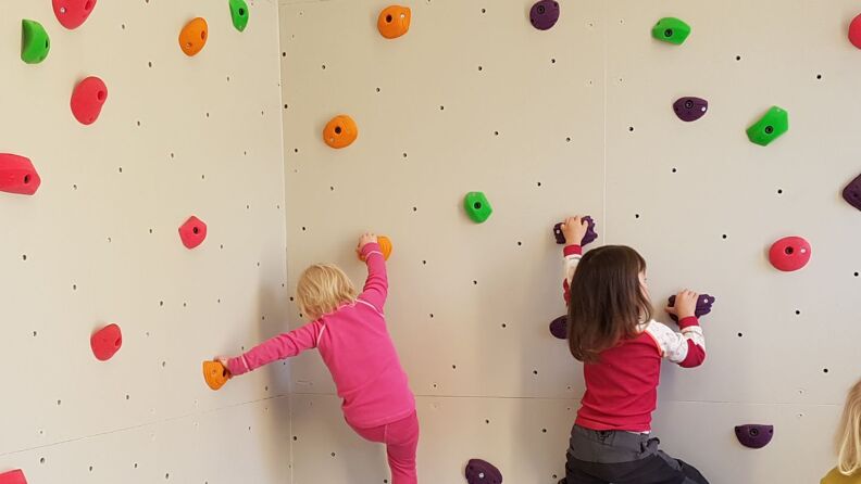 To barn klatrer opp en hvit klatrevegg.