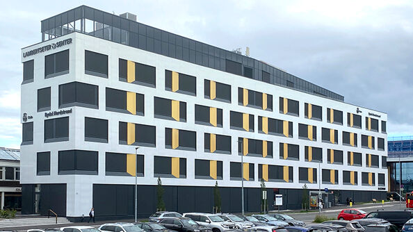 Seksetasjes hvitt kontorbygg, hvor den øverste etasjen er litt lenger inn enn de andre.