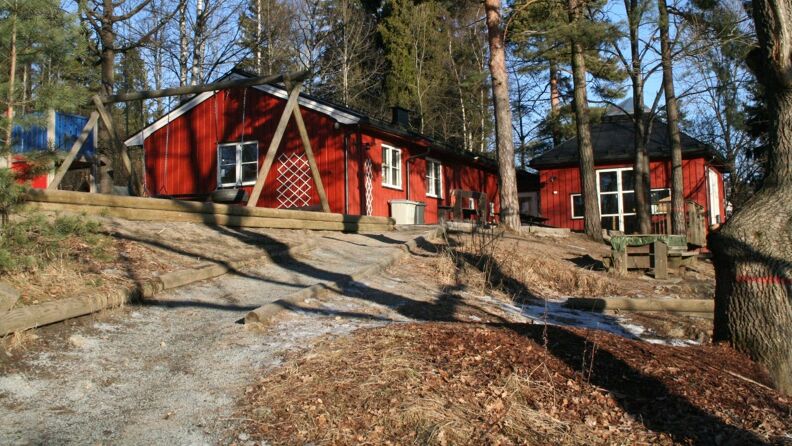 Uteområde med grusvei opp til rødmalt barnehage med huske og trær rundt seg