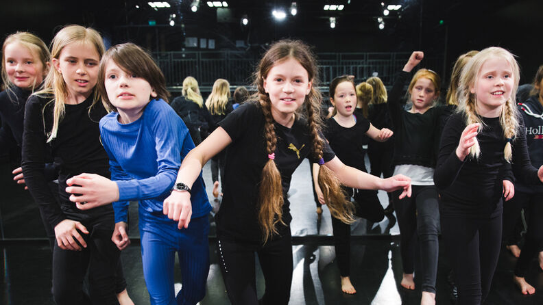 En gruppe teaterelever går i klynge mens de ser inn i kamera, i teatersalen på Schous kulturstasjon.