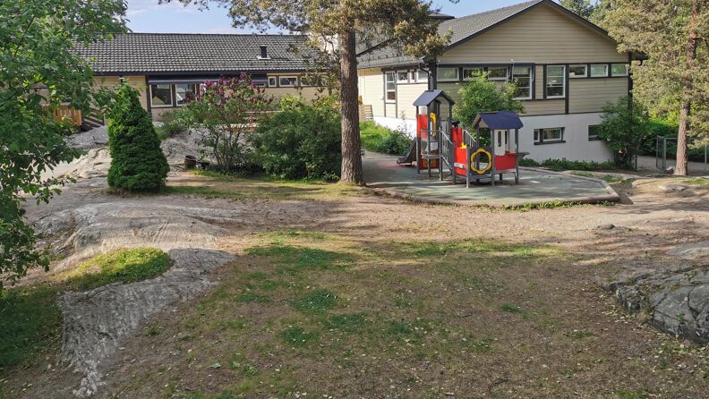 Uteområde utenfor barnehagen med klatrestativ og store grøntområder.