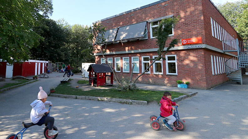 Fasadebilde av barnehagen med barn syklende på trehjulsykkel foran