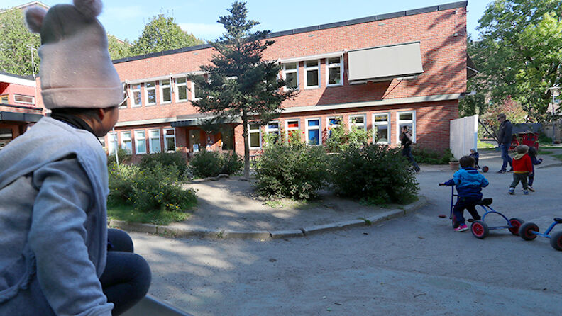 Barn som sitter på lekestiv og ser bort på barnehagebygningen