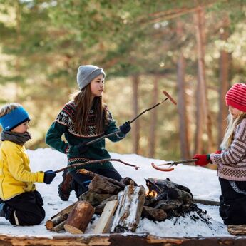Tre barn som griller pølser i skogen på vinteren