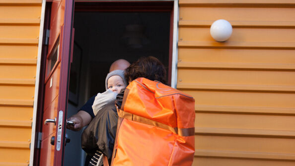 Bildet viser en person som åpen ytterdøren for en annen med barn og bagasje.