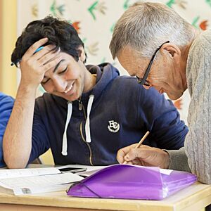 Eldre mann hjelper ung gutt med leksene