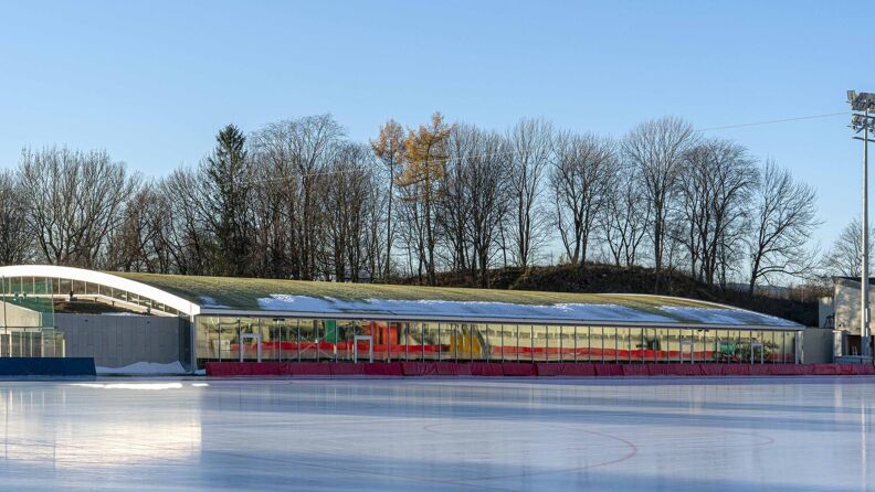 Vinterbilde av Sonja Henie ishall, sett fra utsiden, med en islagt Frogner stadion i forgrunnen.