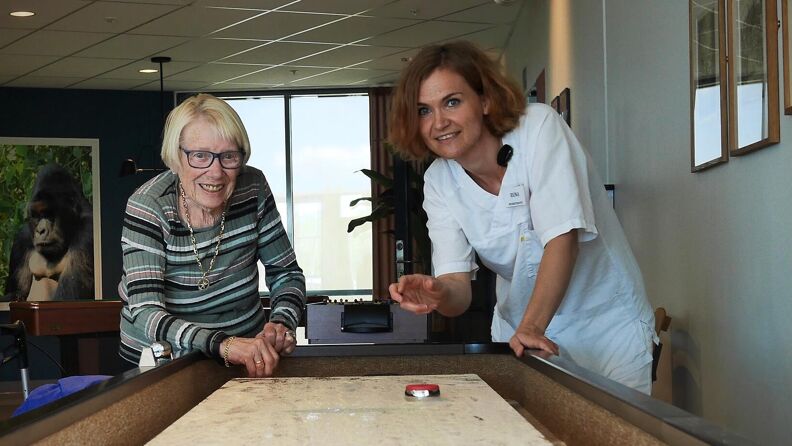 Beboer og ansatt spiller shuffleboard på Lindeberghjemmet