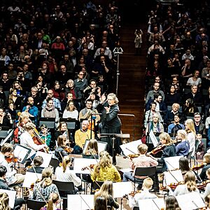 Dirigent omringet av strykere på scenen i Oslo konserthus