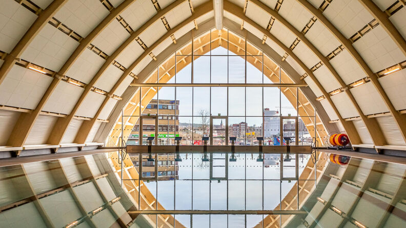 Svømmehallen til Økern bad. Bildet er tatt mot stor glassfasade og gaten utenfor. Refleksjon av vinduet i bassengvannet.  