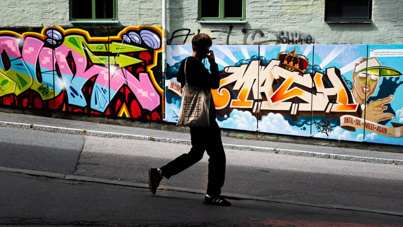 Ungdom gående på vei. Vegg med grafitti i bakgrunnen