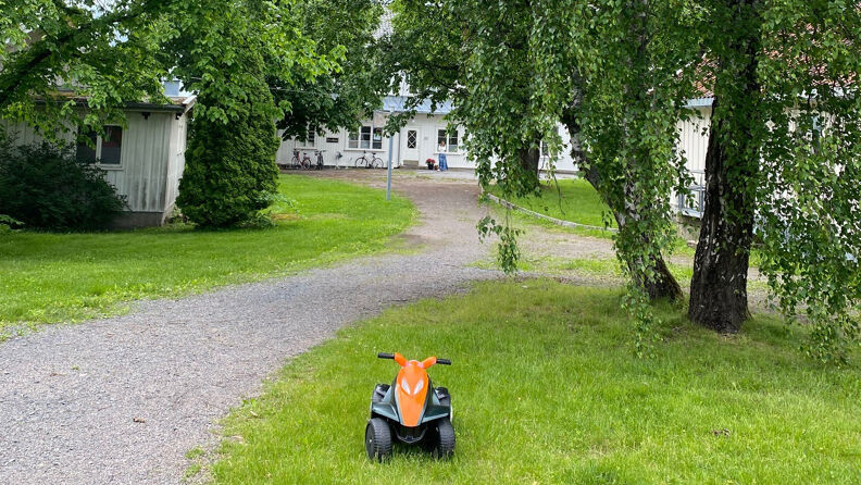 En lekebil står på en gressplen på en gårdsplass. I bakgrunn ser vi et hvitt hus. 