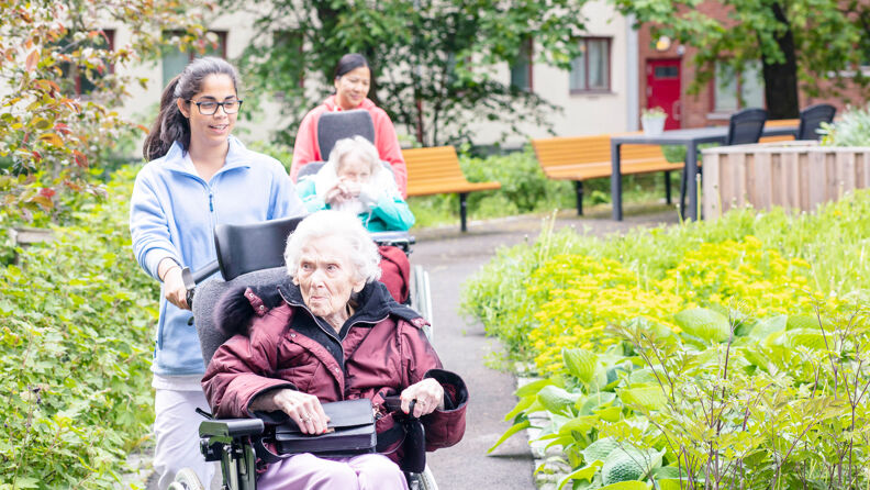 To pleiere går med to beboere som sitter i rullestol i en bakgård til Kingosgate.