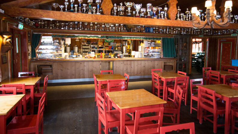 An empty café in the lodge at Ullevålseter. The café looks traditional with dark pine walls and furniture. The chairs are color bright red and the rafters are filled with trophies.