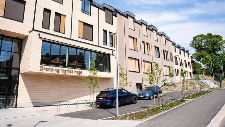 Et bygg med inngangsparti og parkeringsplasser langs bygget. På parkeringsplassene står det to biler. 
